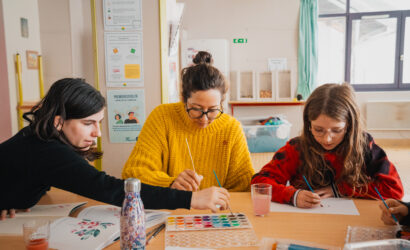 Animatrice à l'écoute d'un·e jeune lors d'une colonie de vacances inclusive, incarnant la pédagogie du care. Le groupe participe à une activité artistique et créative.