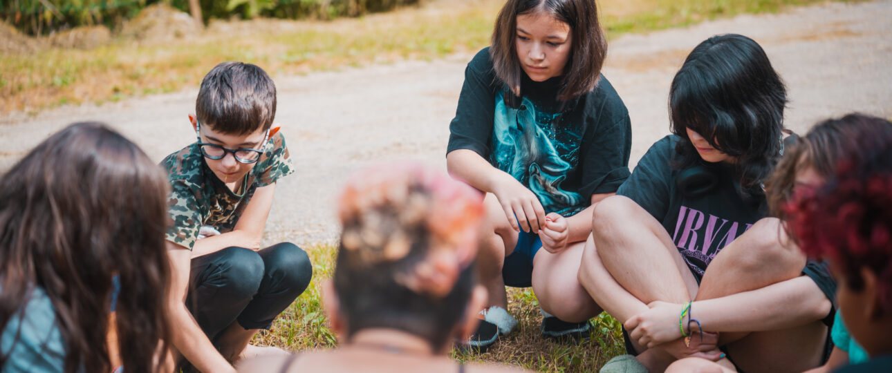 Groupe de jeunes en cercle participant à une assemblée collective lors d'une colonie de vacances écoresponsable