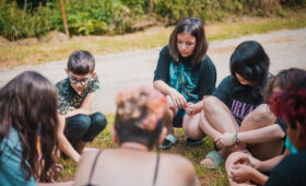 Groupe de jeunes en cercle participant à une assemblée collective lors d'une colonie de vacances écoresponsable